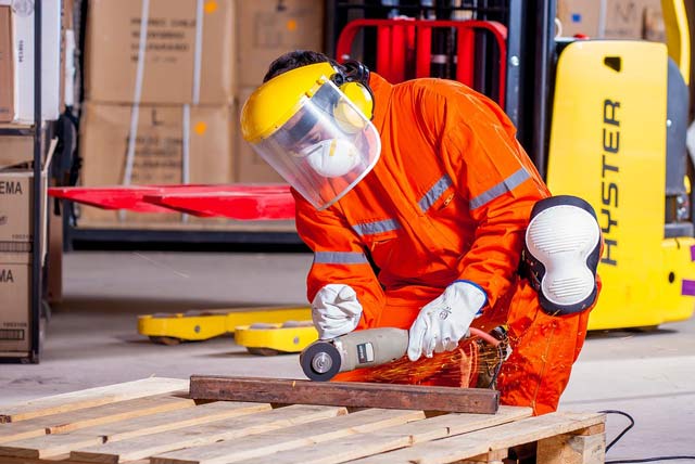 empleado cortando metal con casco y mascarilla